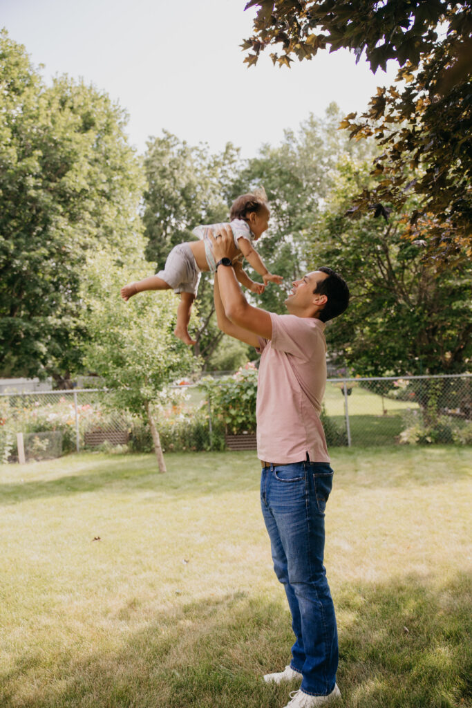Dad playfully tossing baby into the air under a tree during a backyard family photoshoot in Minneapolis