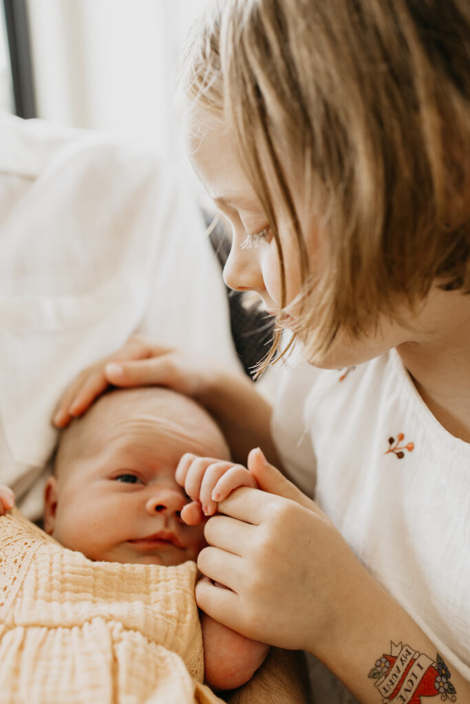Close-up of a big sister holding her newborn sibling's tiny hand during a lifestyle newborn session.