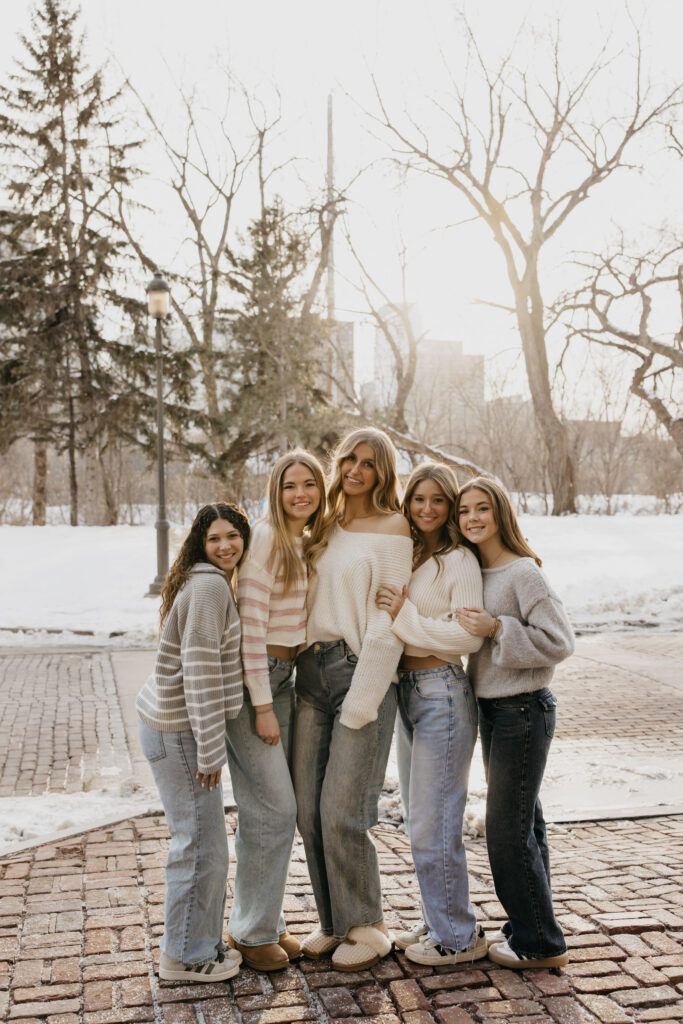 Group of high school senior friends in sweaters and jeans standing on a snowy brick path