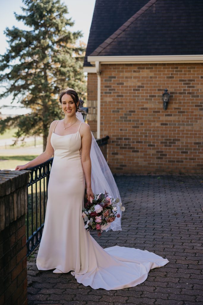 Bride holds her bouquet on a brick patio with her veil and train trailing