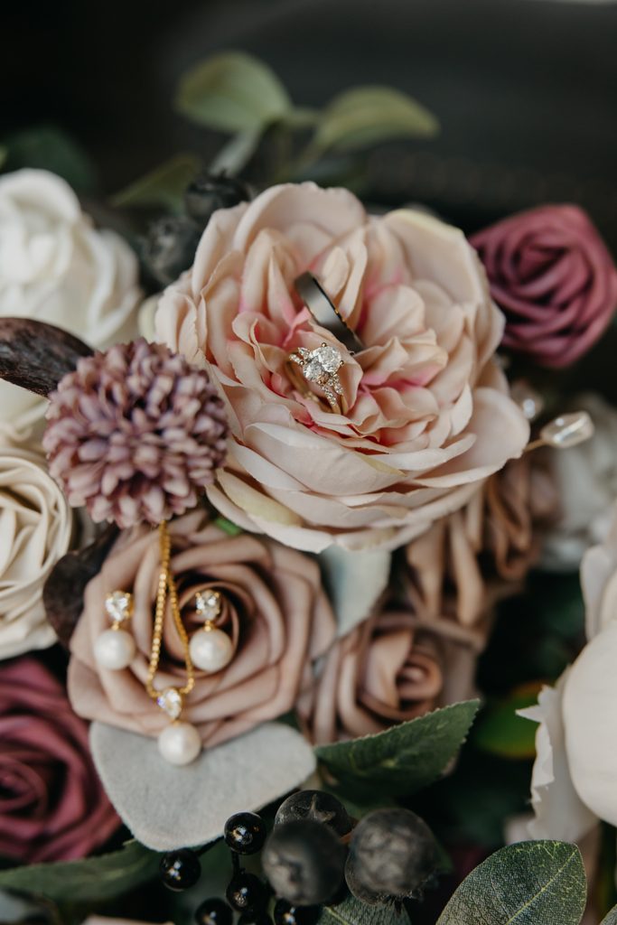 Wedding rings and pearl earrings resting in a bouquet of blush and burgundy flowers