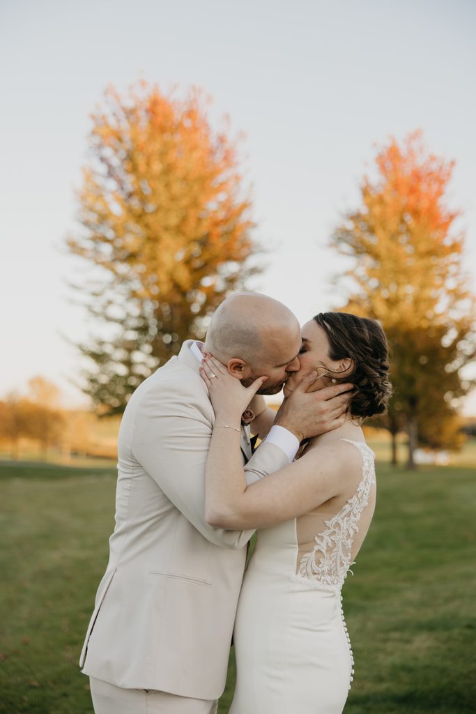 Close-up of bride and groom kissing with orange fall trees behind them