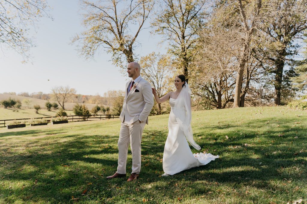 Bride and groom stand apart in a grassy field under bare trees
