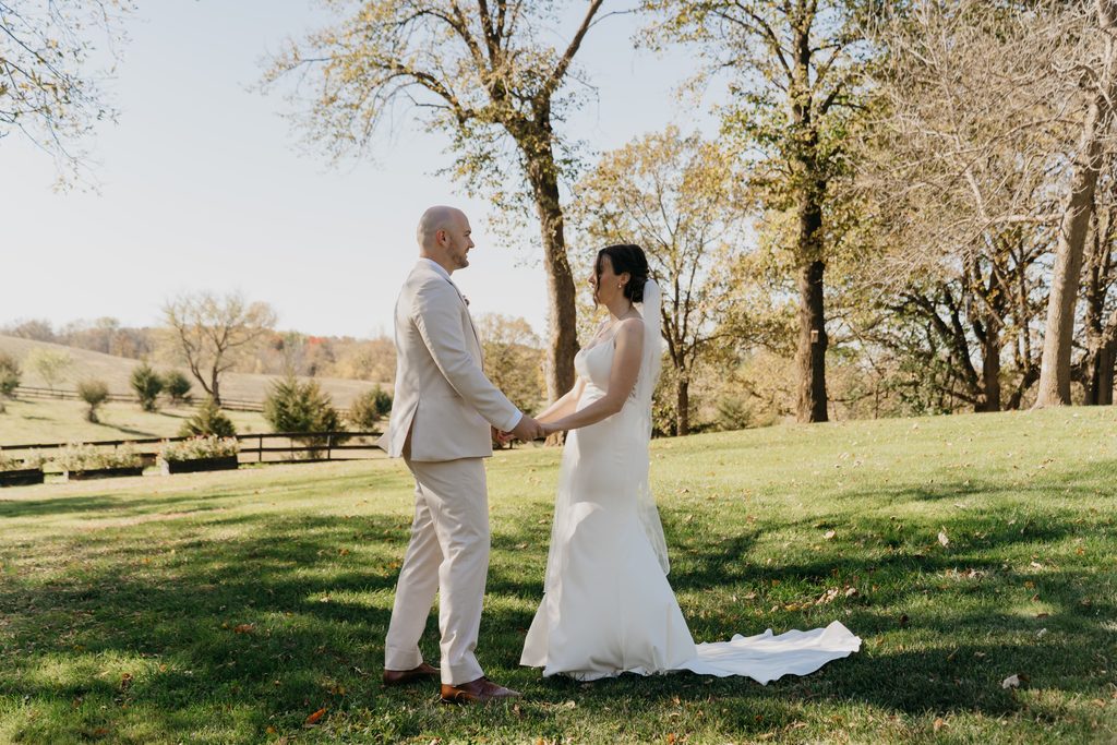 Bride and groom hold hands facing each other in a sunlit field