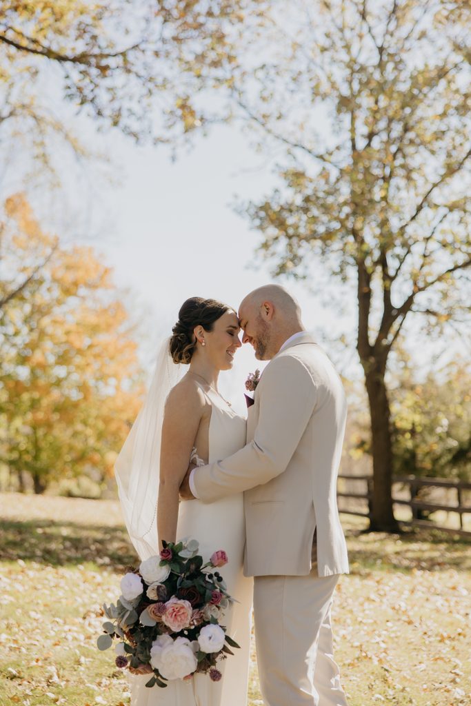 Bride and groom touch foreheads in front of a fall tree with orange leaves