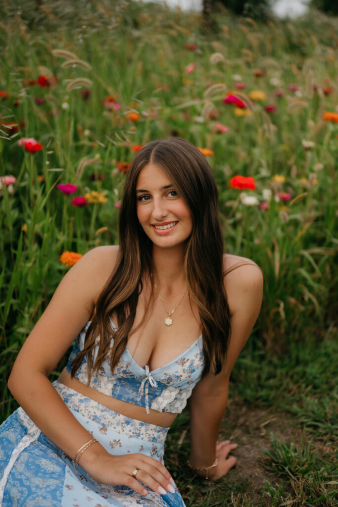 Senior in a blue floral two-piece set sitting in a colorful zinnia field