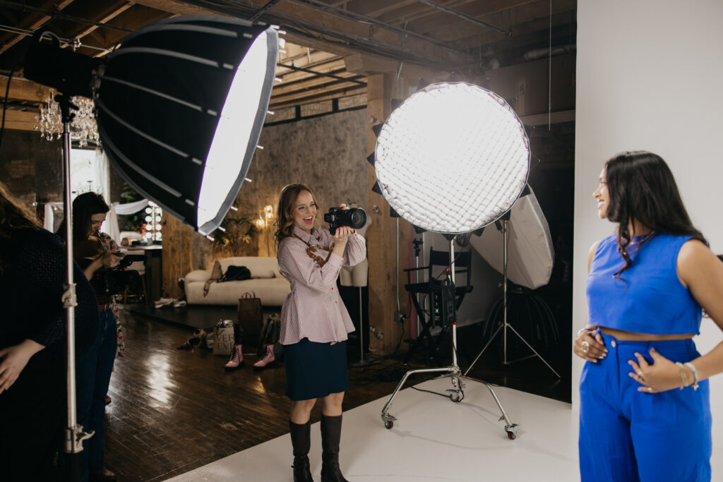 Photographer in a pink striped blouse photographing a client in a blue jumpsuit in studio