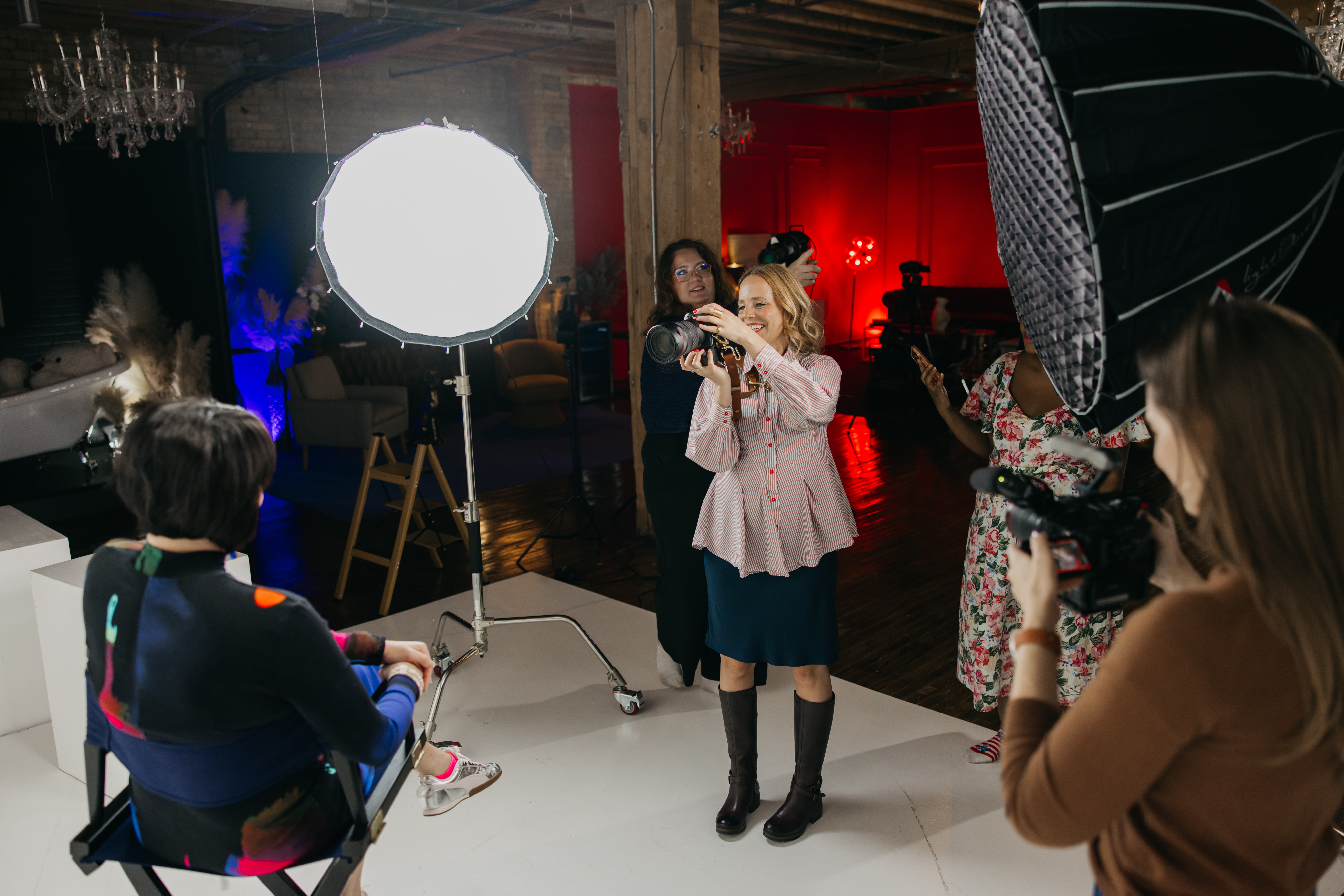 Photographer shooting a seated client under large studio lights while her photography team assists and films behind the scenes
