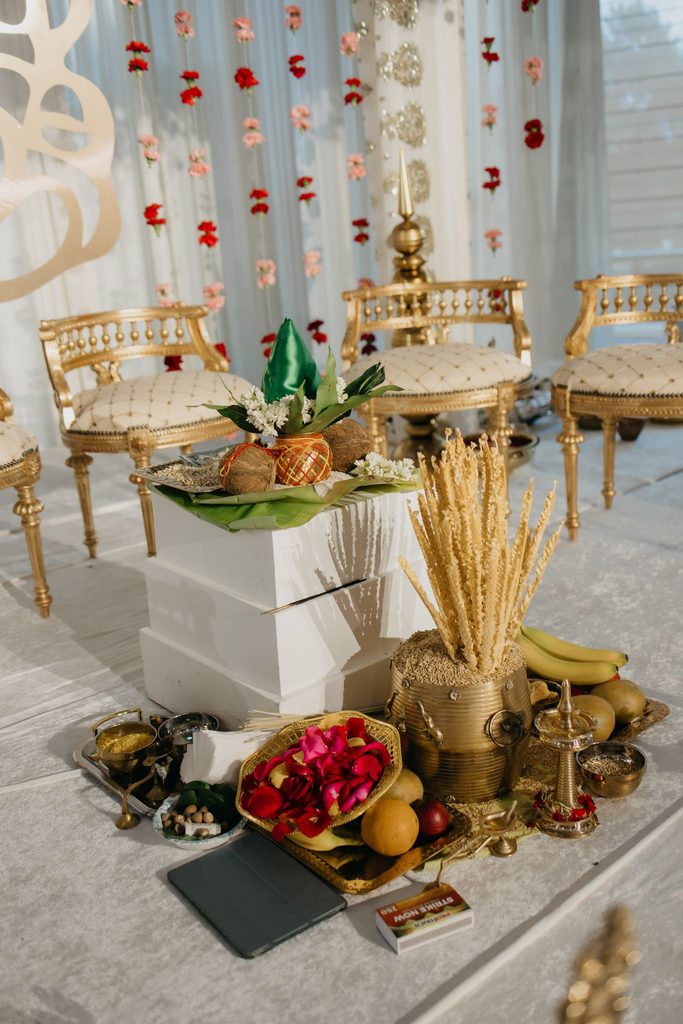 Ceremony setup with gold chairs, fruit, rice stalks, and ritual items arranged on a white platform