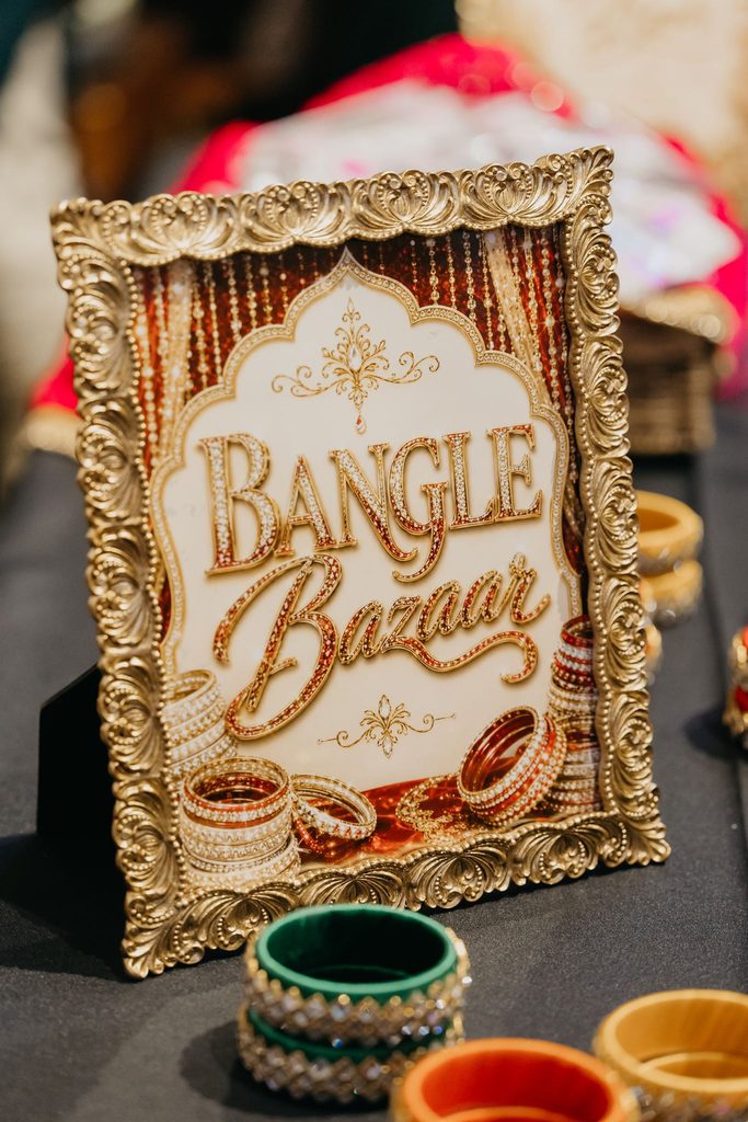 Gold framed “Bangle Bazaar” sign beside colorful bangles on a table at the sangeet