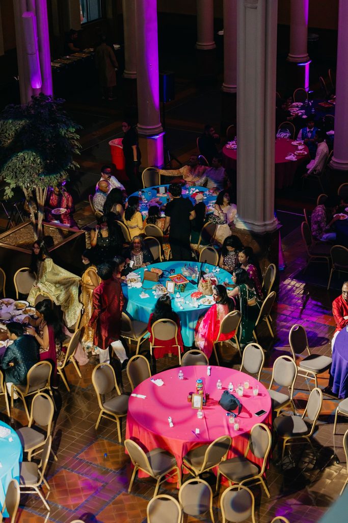 Overhead view of guests seated at pink and teal tables in a ballroom with pink-lit columns
