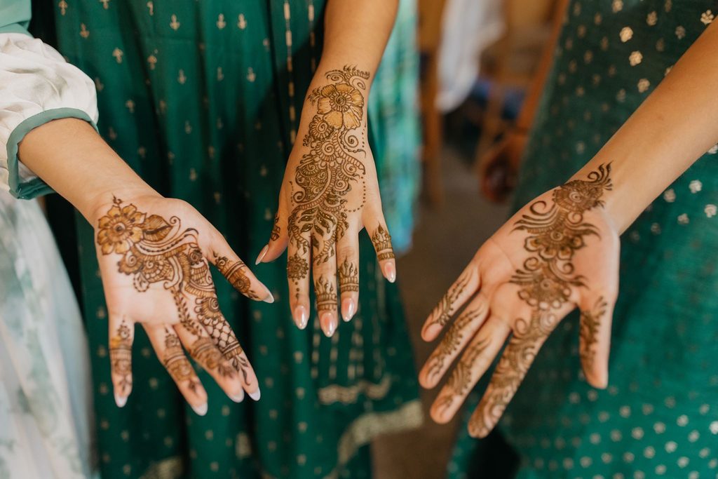 Two women in green outfits show off intricate mehndi designs on their hands
