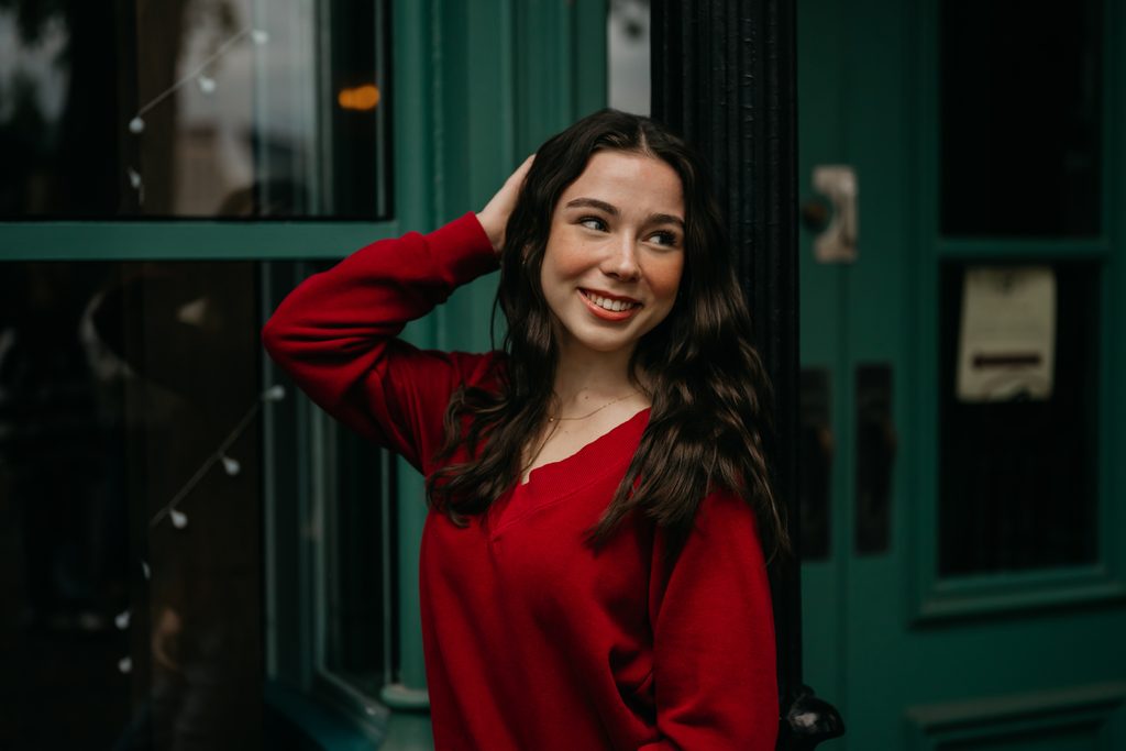 Senior in a red sweater with her hand in her hair in front of a green door