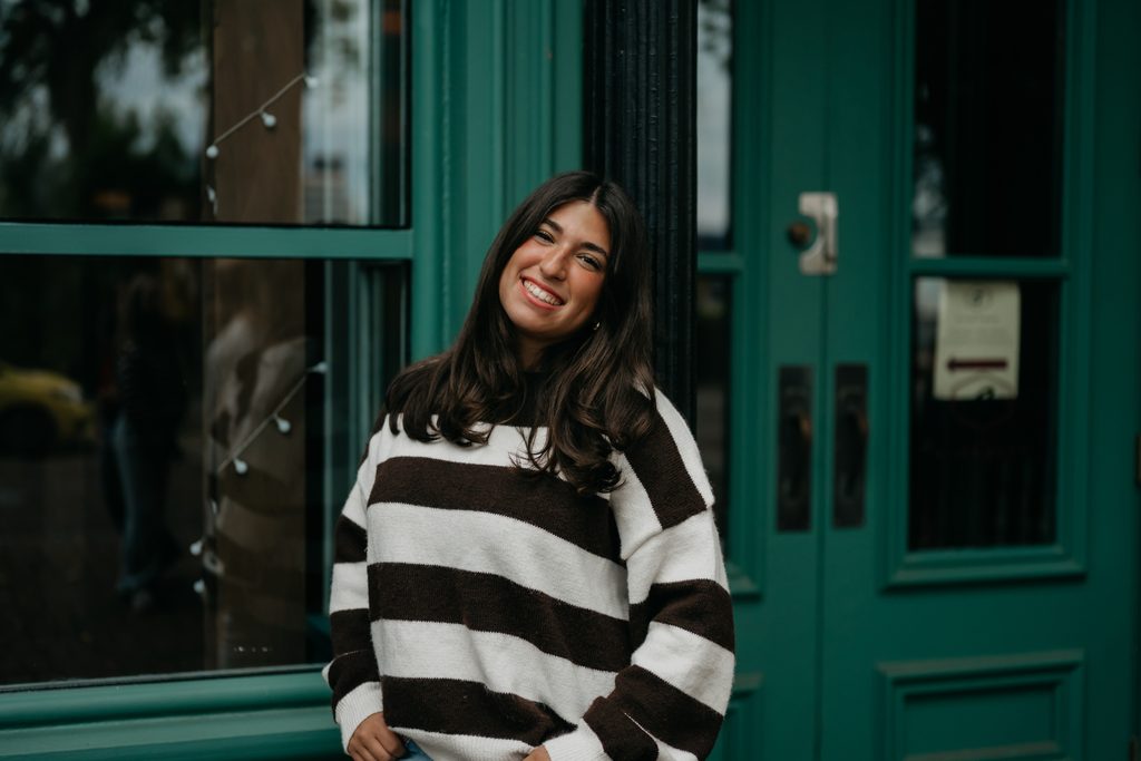Smiling senior in a black and white striped sweater standing in front of a green door