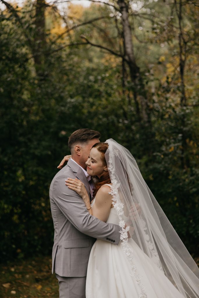 Stephanie and Seth hugging closely among autumn trees, her cheek against his shoulder