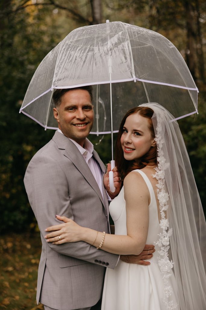 Seth and Stephanie smiling at the camera under a clear umbrella, her veil behind her