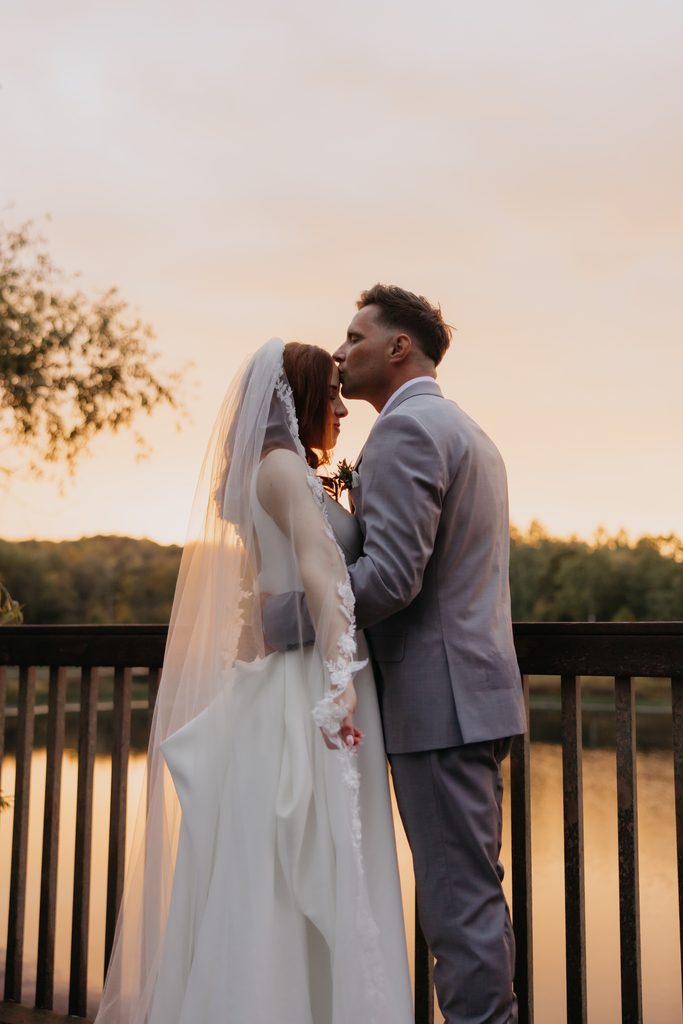 Seth kissing Stephanie at sunset on a lakeside deck, her veil falling over her shoulder