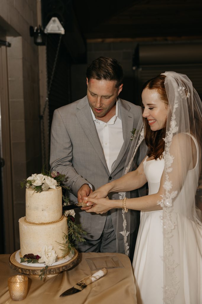 Seth and Stephanie cutting their white wedding cake together at night