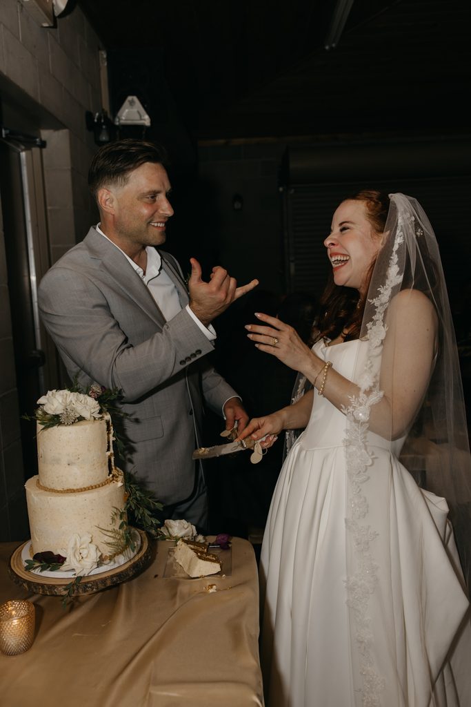 Seth and Stephanie laughing together beside their white wedding cake