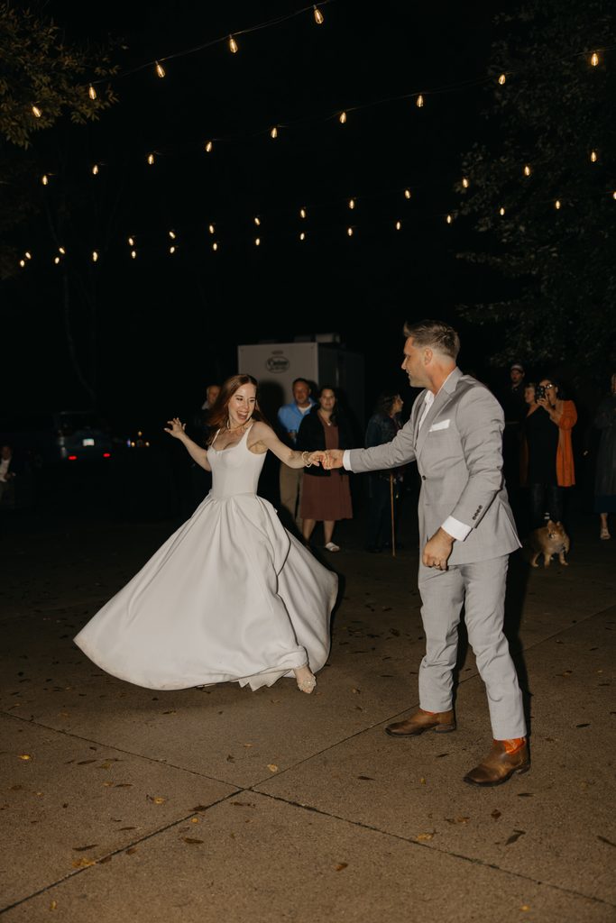 Stephanie twirls in her gown while Seth holds her hand during their dance under string lights