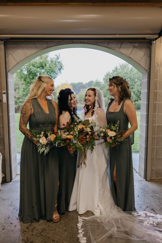 Stephanie laughing with her bridesmaids in olive green dresses inside a stone archway
