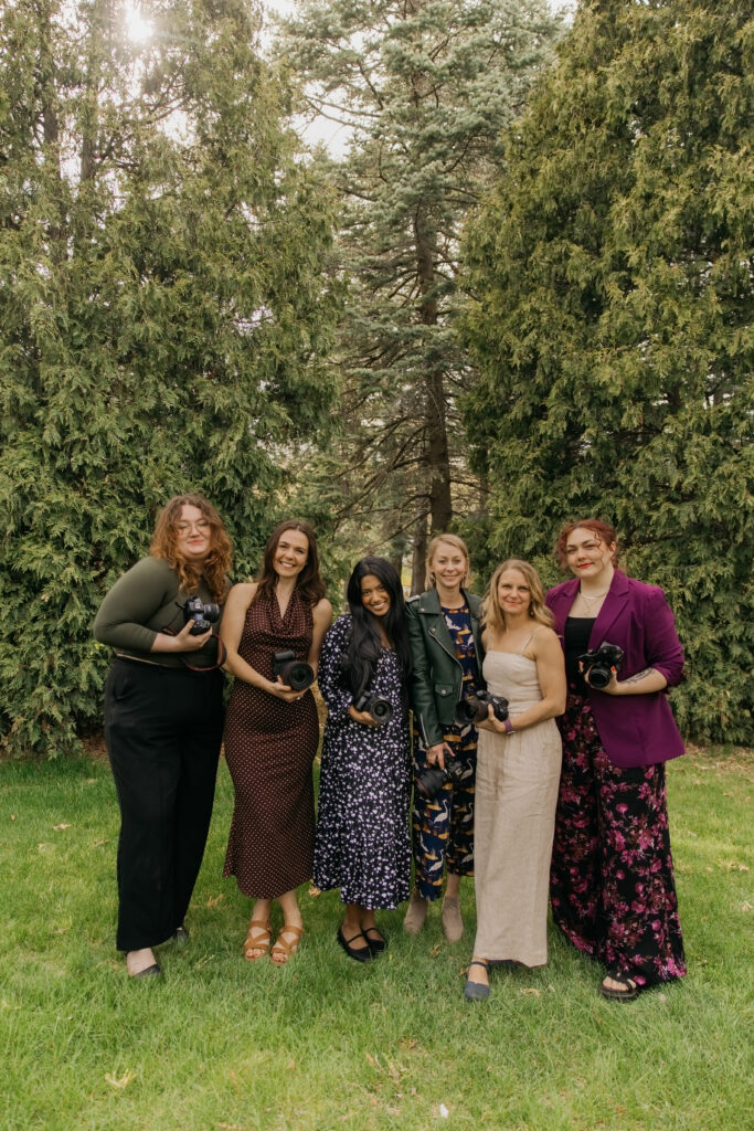 Six team photographers standing close together and smiling, each holding her camera