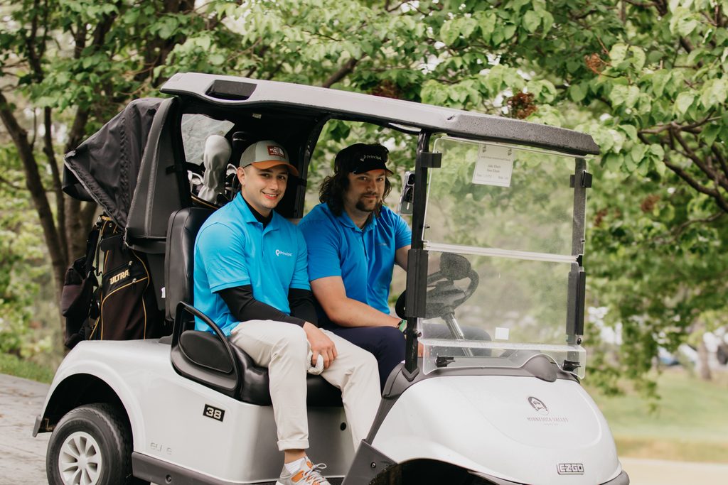 Two men in matching blue polos smiling from a golf cart