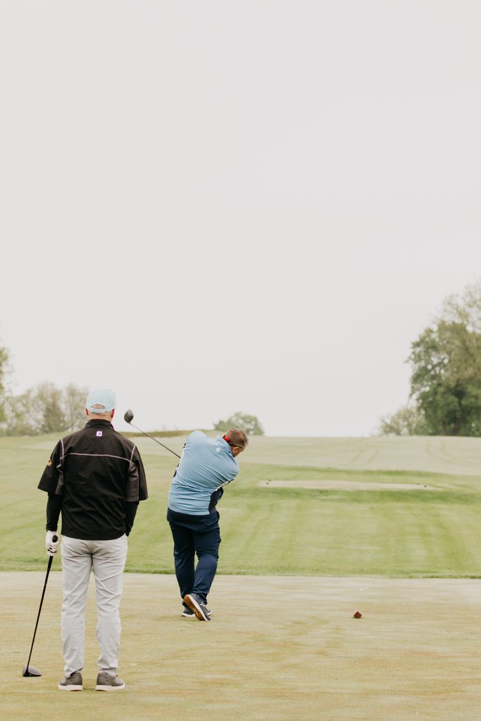 Golfer mid-swing on the tee while a second golfer watches