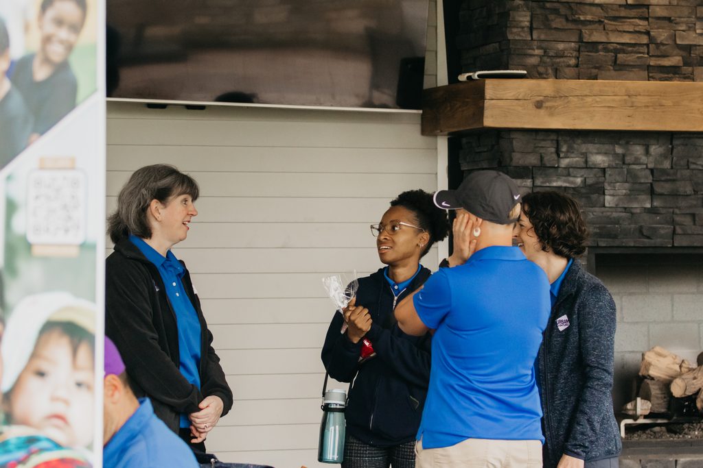Volunteers and a guest talking on a covered patio beside a stone fireplace and a banner