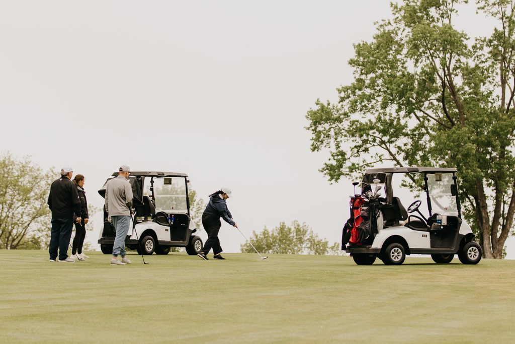 Golfers and a golf cart on the fairway under an overcast sky