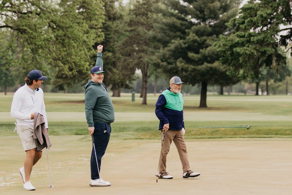 Three golfers on the green, one raising an arm in celebration