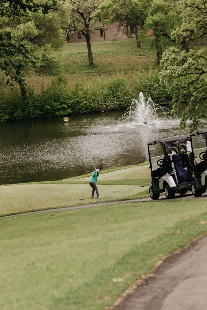 Golfer on the fairway near a pond with a fountain and a parked golf cart