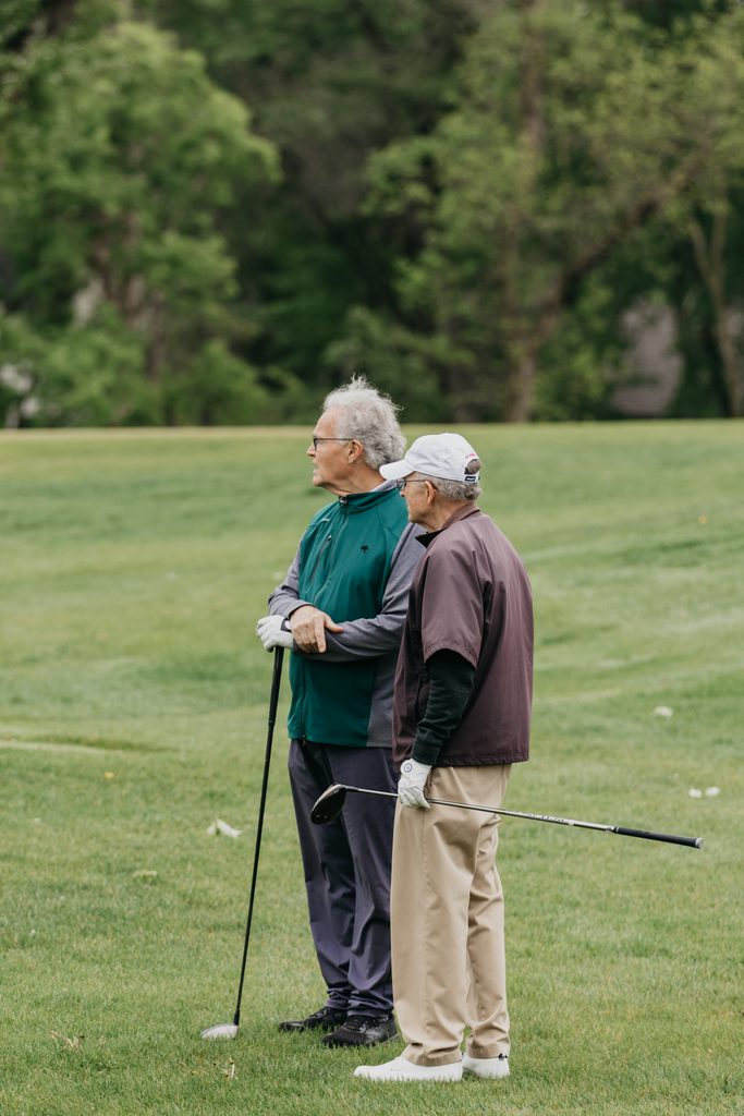 Two older golfers standing on the fairway holding clubs and talking