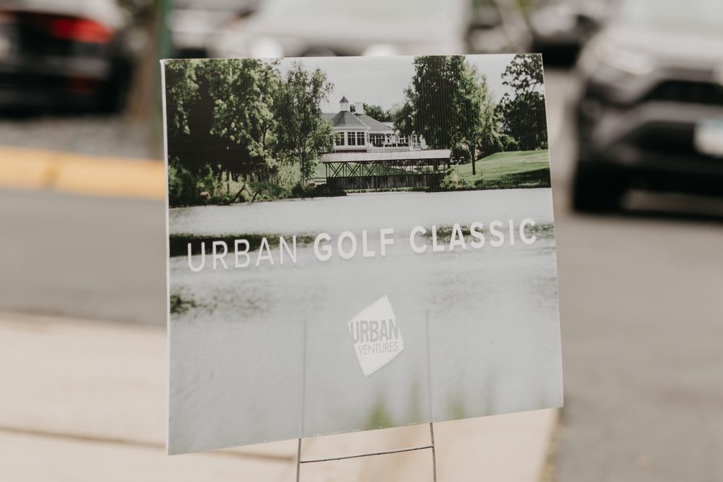 “Urban Golf Classic” sign with the Urban Ventures logo and a clubhouse image on a stand