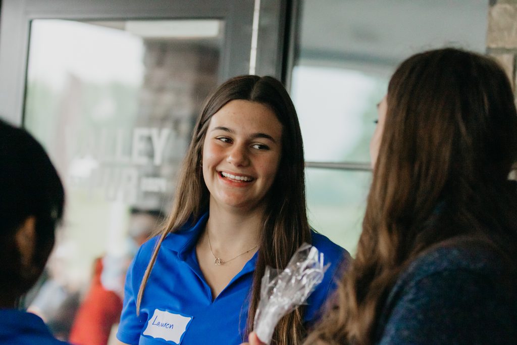 Smiling young volunteer in a blue polo holding a small bag, name tag on her shirt