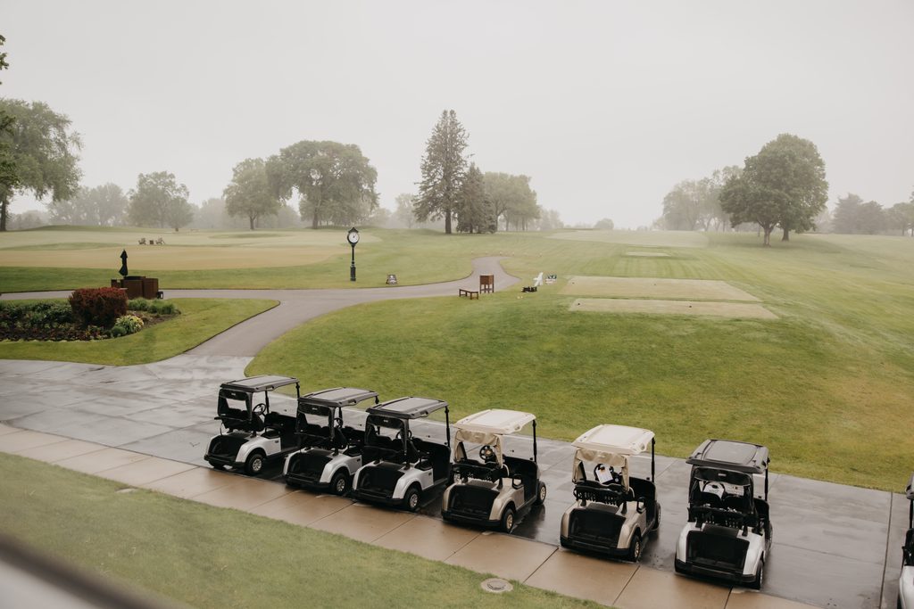 Row of golf carts parked beside a putting green on an overcast day