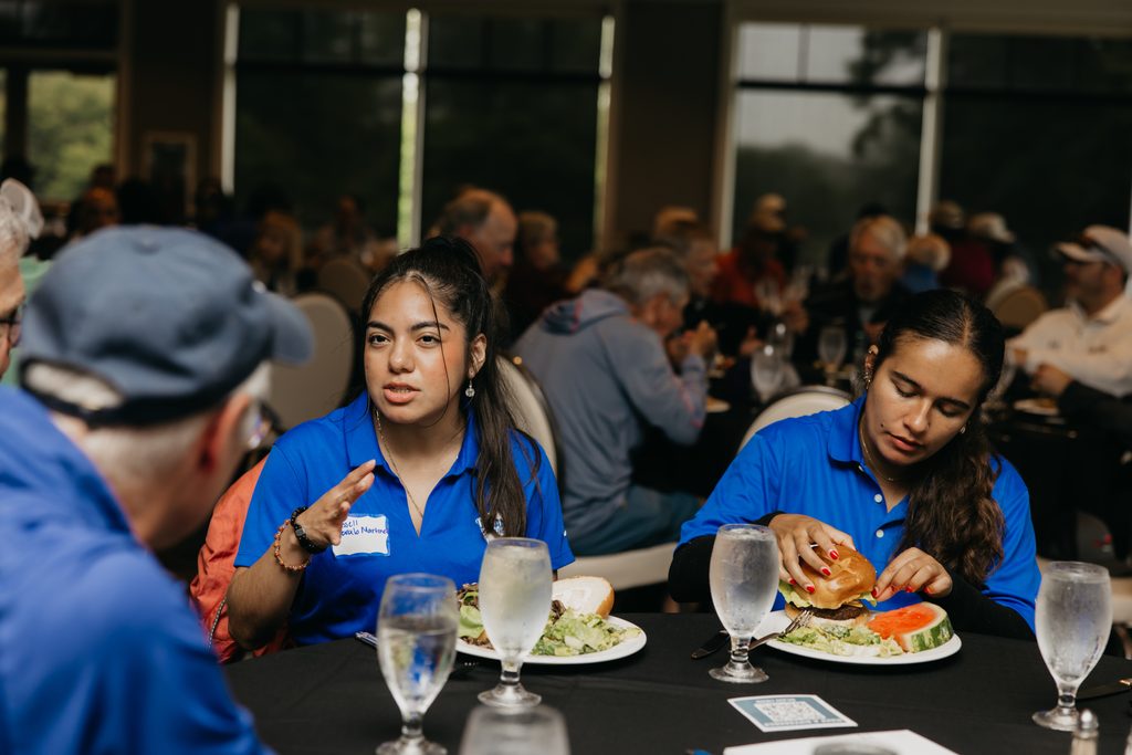 Two young volunteers in blue polos eating burgers at a lunch table