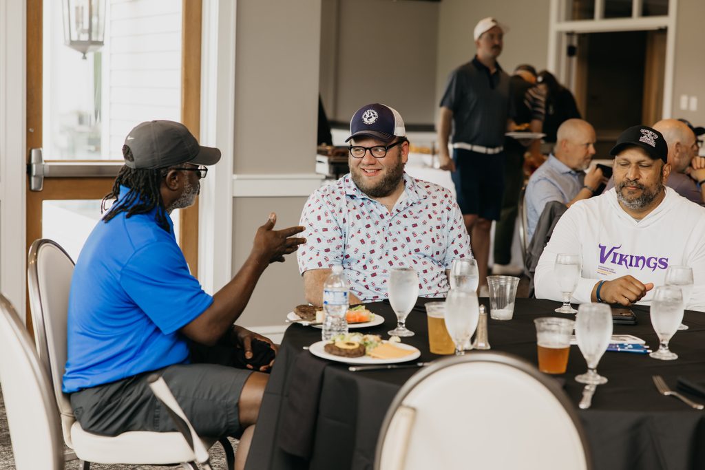 Volunteer talking with two guests at a ballroom table, one in a patterned shirt and one in a white sweatshirt