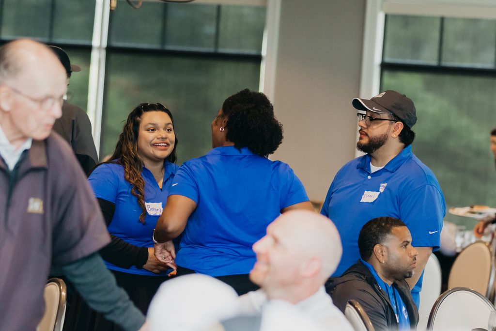 Smiling volunteers in blue polos seated with guests at lunch tables