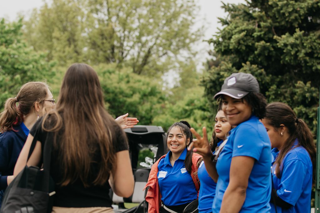 Urban Ventures volunteers in blue polos chatting outdoors, one in a gray cap smiling