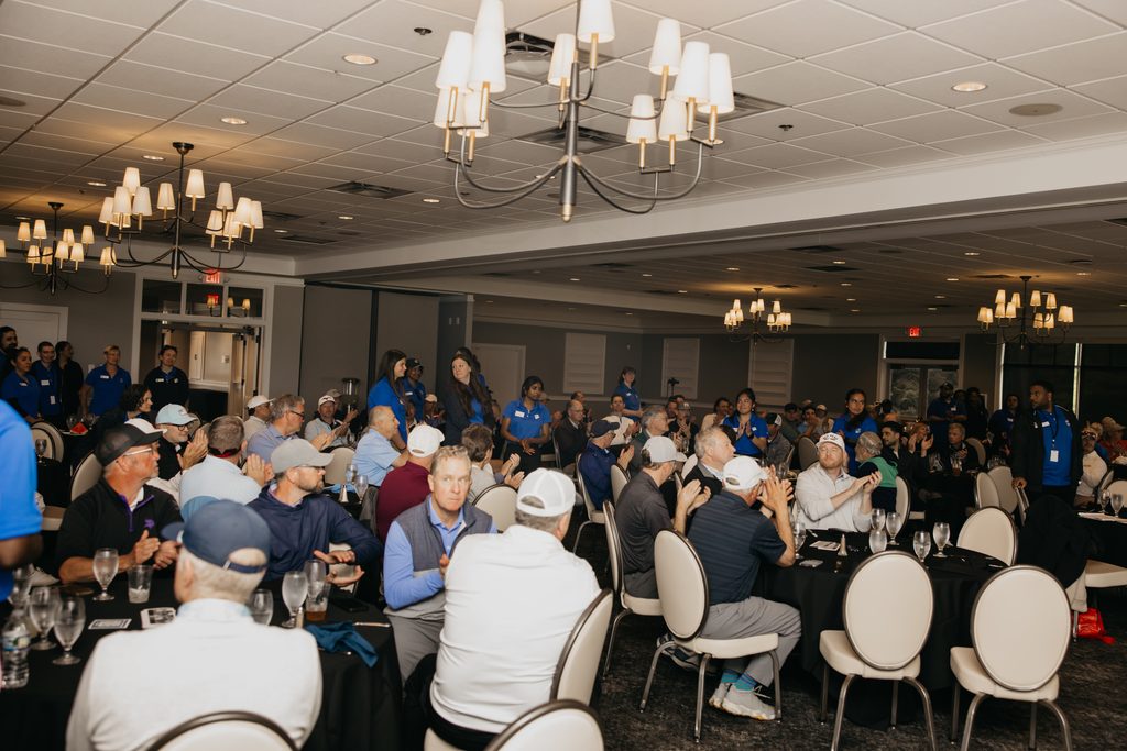 Wide view of a ballroom filled with guests at round tables under chandeliers