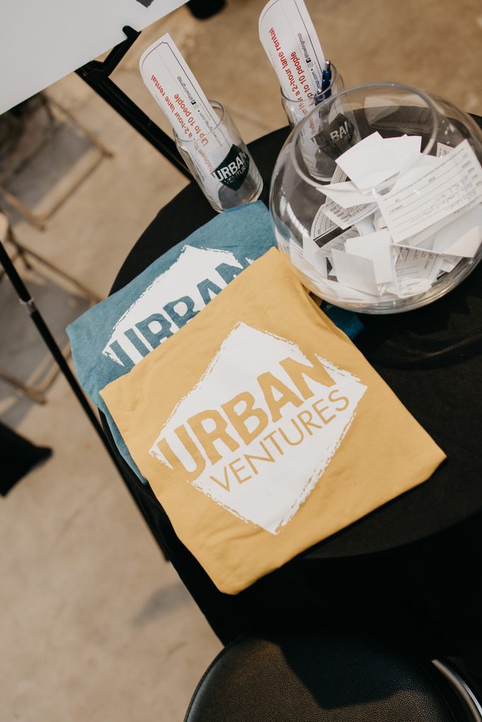 Folded Urban Ventures t-shirts rest on a table beside a glass bowl of raffle tickets